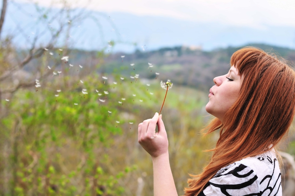 girl blowing on dandelion outdoors